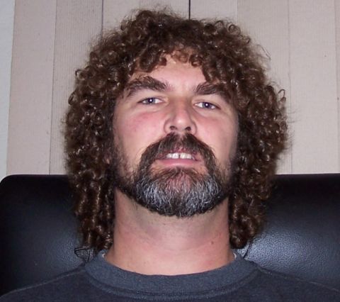 1990 Ford Bronco - A man with a beard and curly hair is shown from the chest up, seated in a dark chair.