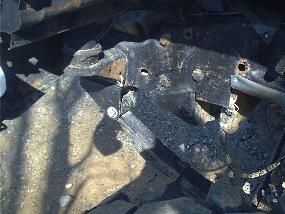 Close-up of rusted metal brackets and bolts on a vehicle's frame, with shadows cast on the ground