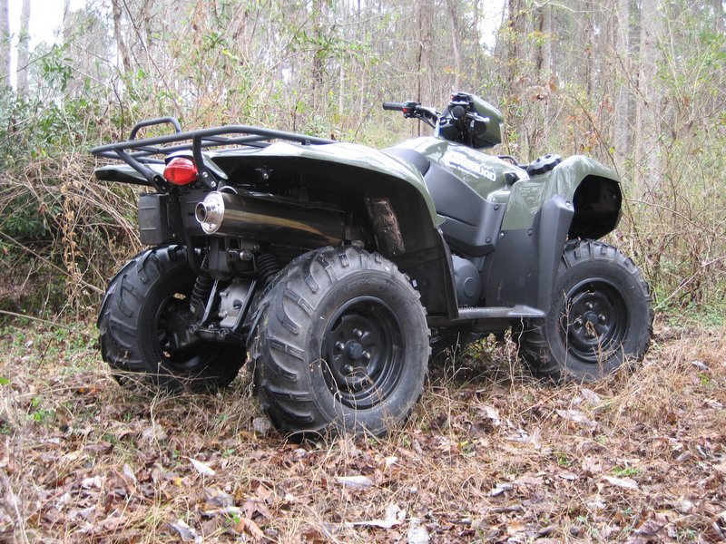 Olive green utility ATV parked in leafy woods, rear three-quarter view