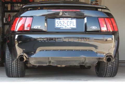 1986 Ford Bronco - Black 2003 Ford Mustang GT shows its rear end with dual exhaust and a spoiler.