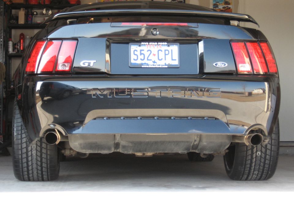 Rear view of a black 2003 Ford Mustang GT with dual exhaust pipes and a spoiler