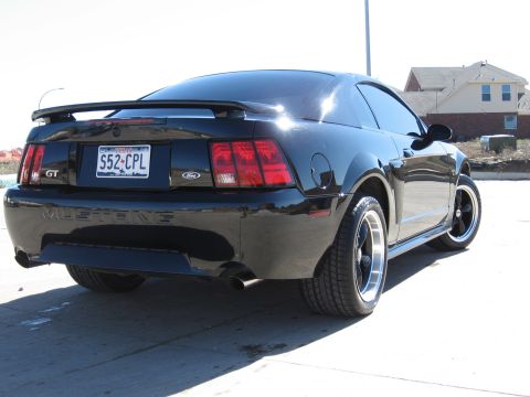 1986 Ford Bronco - This black Ford Mustang GT shows its rear end with a spoiler and custom wheels.