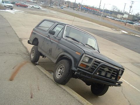 1986 Ford Bronco - This black SUV is positioned with its front passenger wheel on a curb, displaying its grille and a 3/4 front view.