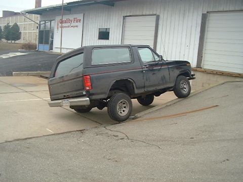 1986 Ford Bronco - Side view of a 1986 Ford Bronco on a sloped surface near a commercial building.