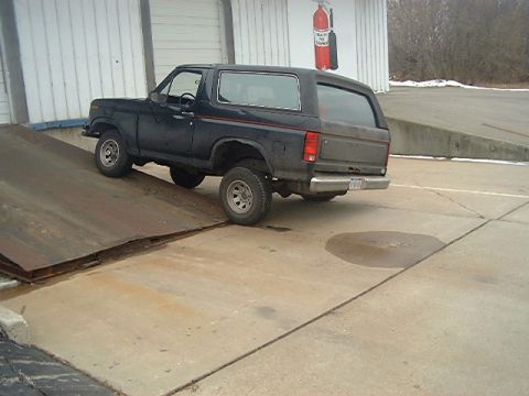 1986 Ford Bronco - A dark blue Ford Bronco is positioned on a metal ramp outside a building.