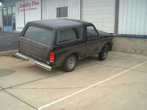 1986 Ford Bronco - This black SUV, likely from the 1980s, is parked in front of a building with 'Quality Fire Equipment Company' signage.
