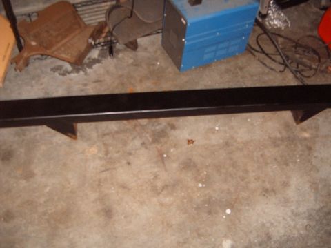 1988 Ford Bronco - A black metal bumper sits on a concrete floor, with a blue welding machine and other parts visible in the background.