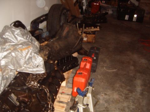 1988 Ford Bronco - Various automotive parts, including an engine block, transmission, and a tire, are stored in a garage setting.