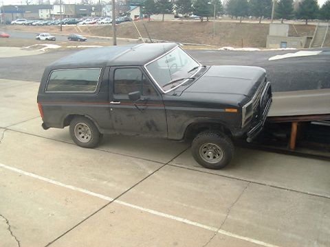 1986 Ford Bronco - Black 1980s Ford Bronco parked outdoors next to a large covered object.