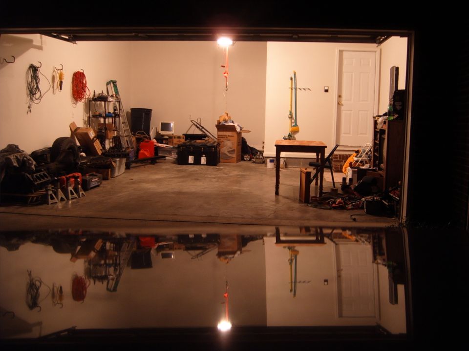 Garage interior with tools, storage shelves, a computer monitor, and a table. Floor is wet and reflective
