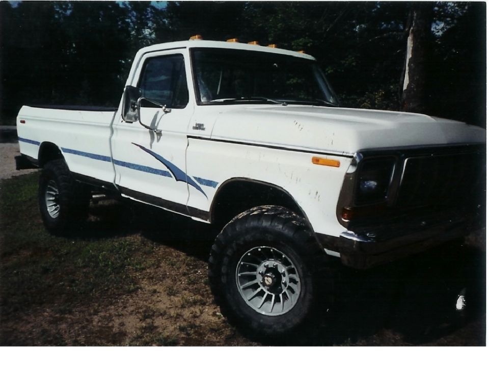 White pickup truck with blue graphics on the side, lifted suspension, and aftermarket wheels