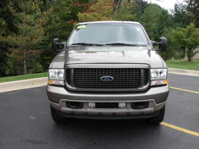 Front view of tan 2002 Ford Excursion SUV in parking lot with trees behind