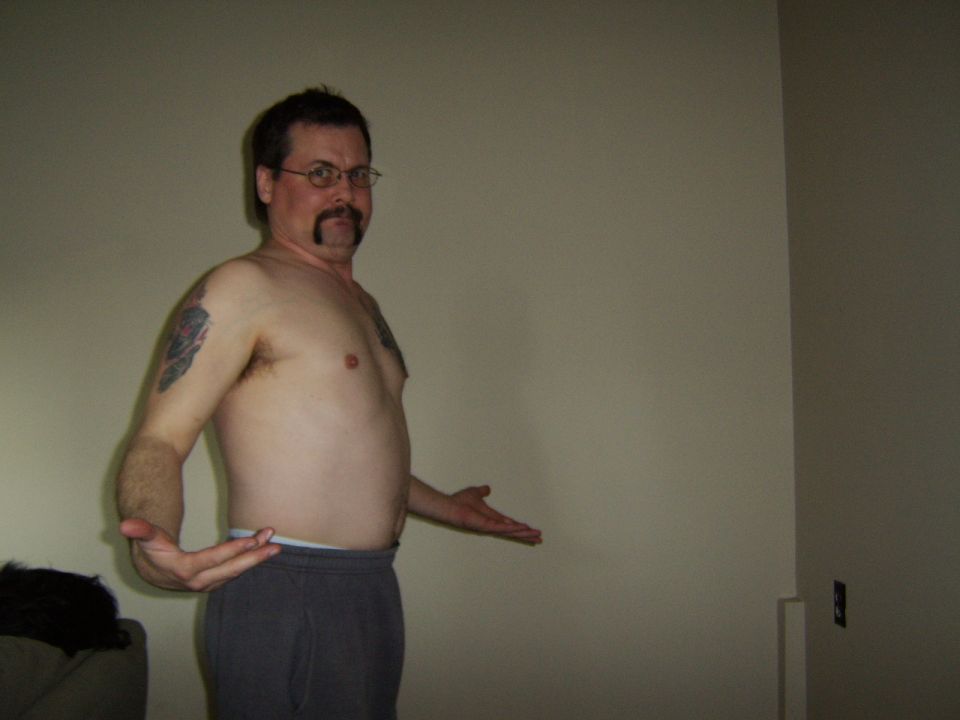 Man with mustache, glasses, and tattoo on arm, wearing sweatpants