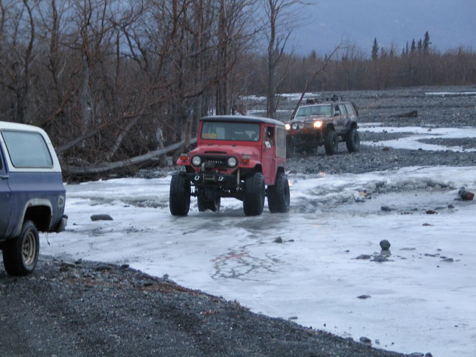 Red Toyota Land Cruiser FJ40 with winch driving through icy water, front view