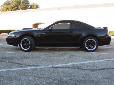 1986 Ford Bronco - Side profile of a black 2003 Ford Mustang GT coupe with aftermarket wheels.