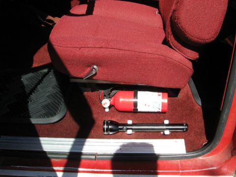 1986 Ford Bronco - Interior view of a vehicle shows a fire extinguisher and flashlight secured beneath the passenger seat.
