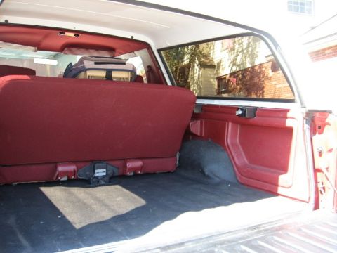 1986 Ford Bronco - The interior cargo area of a vehicle features red upholstered seats and black carpeting, with a cooler visible on the rear seat.