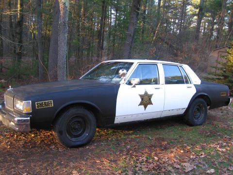 1991 Ford LTD Crown Victoria - A two-tone police car with 'SHERIFF' text and a star badge is parked outdoors.