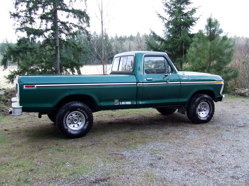 Green 1977 Ford F-150 pickup truck parked on gravel and grass, side view