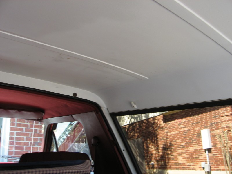 Interior view of a vehicle's headliner and upper door frame, with a brick building visible through the window