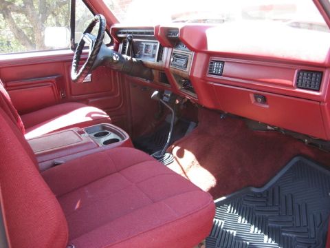 1986 Ford Bronco - The interior of a red truck features a dashboard with a radio and climate controls, a steering wheel, and plush red seats.