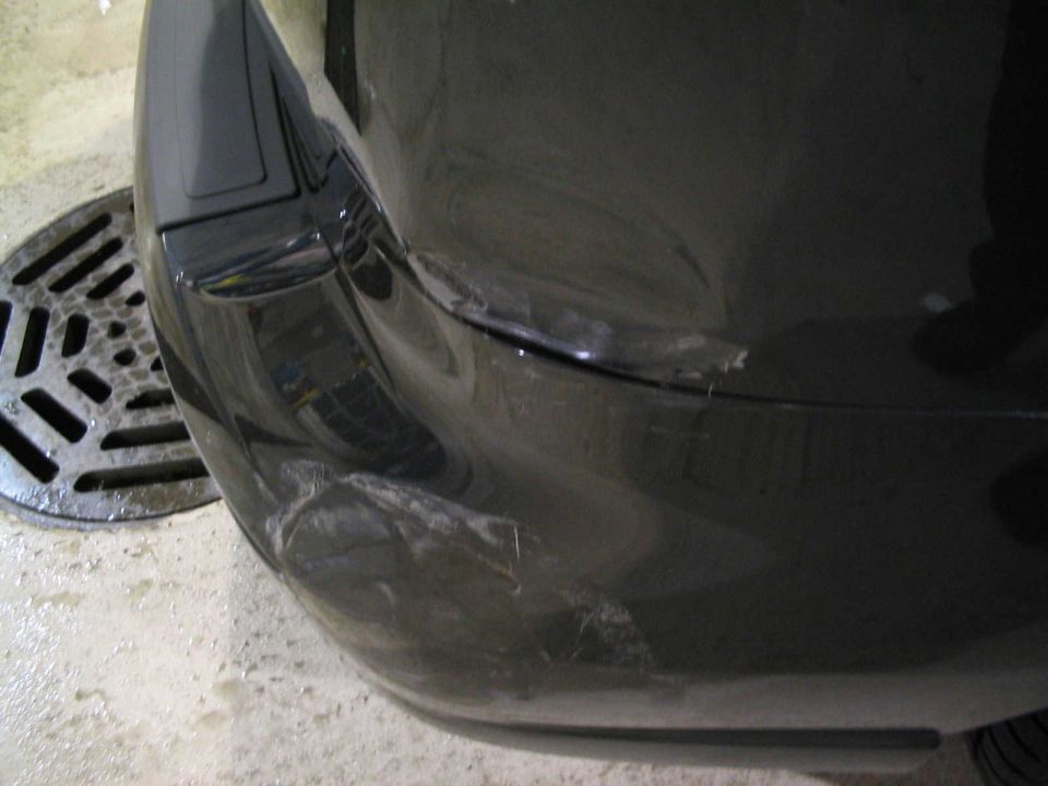 Scraped and creased rear bumper corner damage on a dark gray car