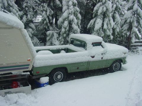 1986 Ford Bronco - A snow-covered green pickup truck is parked next to a trailer in a snowy environment.