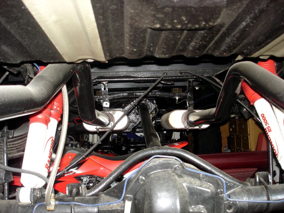 Underside view of a truck's rear axle, dual exhaust, and red Rancho RS 5000 shocks
