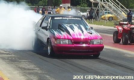 1963 Ford Fairlane - A pink Ford Mustang performs a burnout on a drag strip, surrounded by smoke.
