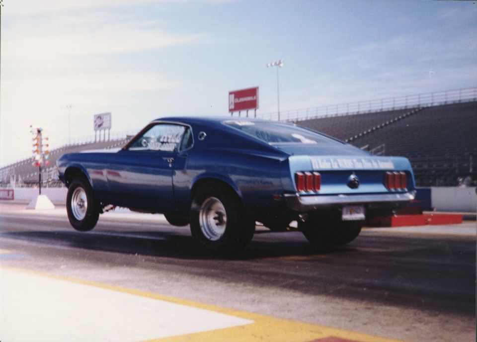 Blue 1969 Ford Mustang drag car launching off the line, rear view