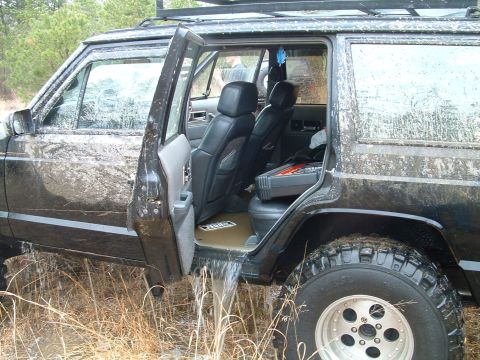 1994 Ford Bronco - A muddy Jeep Cherokee XJ has its doors open, with water flowing out onto the ground.