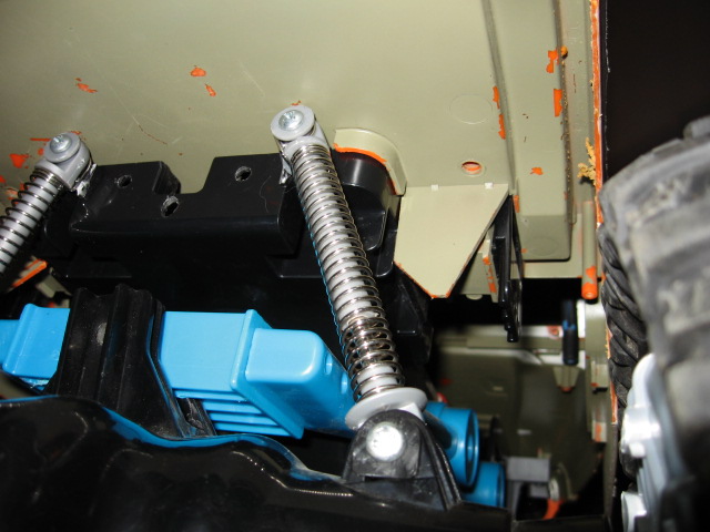 Close-up of vehicle suspension with springs, black and blue plastic parts, and metal brackets. Some orange paint is visible