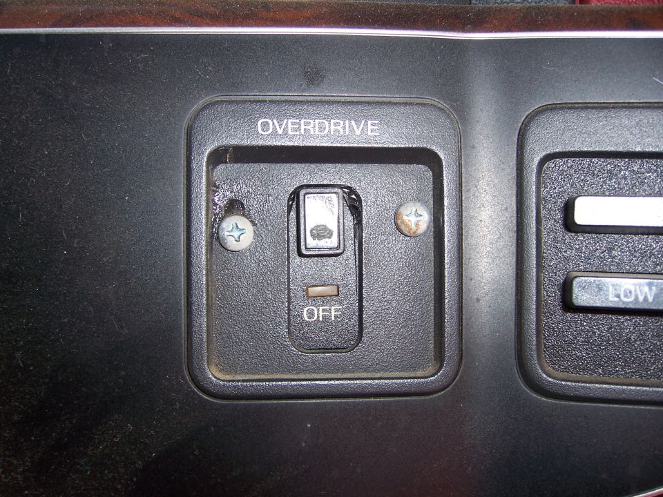 Close-up of a vehicle's dashboard showing an overdrive off switch and part of climate controls