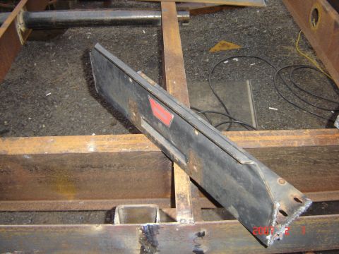 1993 Ford Bronco - A black metal bumper part is shown mounted on a rusty metal frame, with visible wiring and debris on the ground.