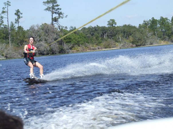 Water-skier in red vest crossing a blue lake, wooded shore behind
