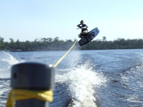 1998 Moomba Boomerang - Wakeboarder performing a jump on a sunny day. "SUPER MOTORS" logo is visible.