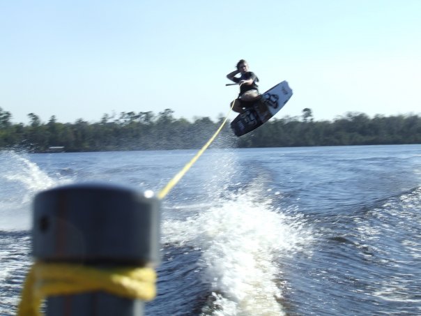 Wakeboarder airborne off a boat wake with the yellow tow rope on the tower pylon
