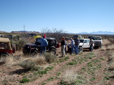 1996 Ford Bronco - A group of people stand around several off-road vehicles on a dusty trail under a clear blue sky.