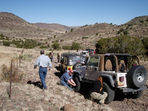 1996 Ford Bronco - Several Jeep Wranglers are stopped on a dirt trail in a dry, hilly landscape as people attend to the vehicles.