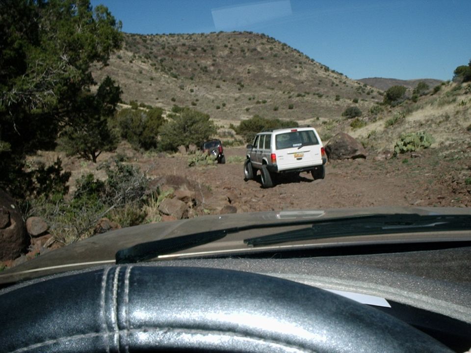 Two SUVs driving on a dirt trail in a desert landscape with hills and sparse vegetation