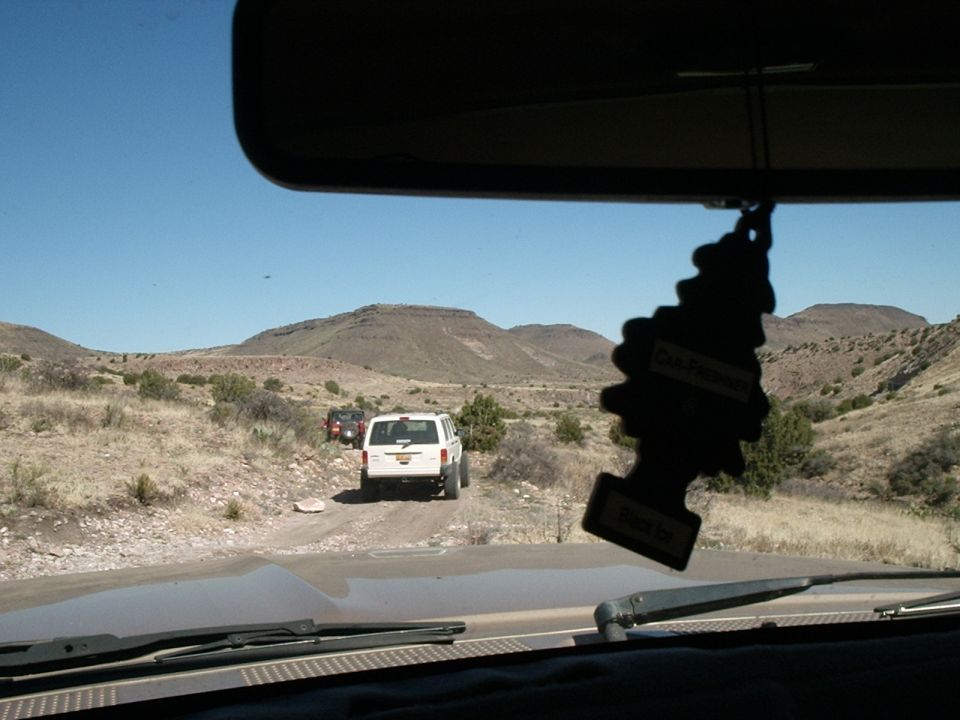 White SUV on dirt road, mountains behind. Two other vehicles visible
