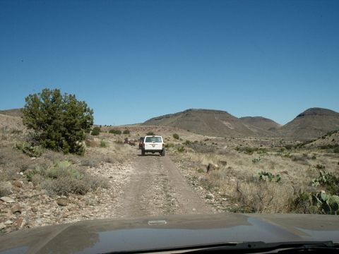 1996 Ford Bronco - White Ford Bronco on a dirt road in a desert landscape with other vehicles ahead.