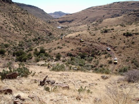 1996 Ford Bronco - Several off-road vehicles navigate a winding dirt path through a dry, mountainous landscape.