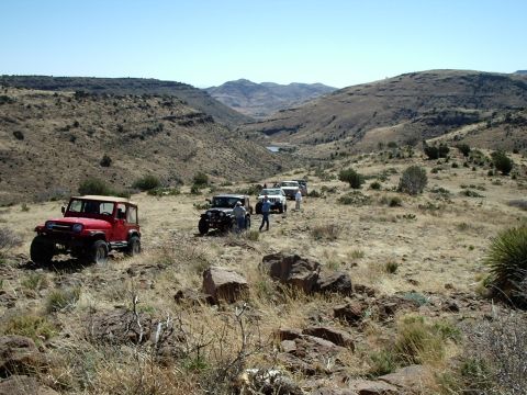 1996 Ford Bronco - A group of Jeeps navigates a , arid terrain under a clear blue sky.