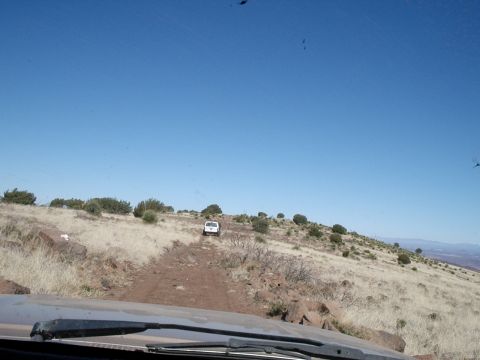 1996 Ford Bronco - Two SUVs navigate a dry, grassy hillside on a dirt trail under a clear blue sky.