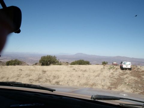 1996 Ford Bronco - Two SUVs navigate a dry, grassy terrain with distant mountains under a clear blue sky.