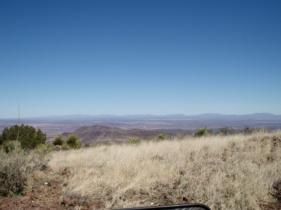 Mountain landscape with dry grass in the foreground and distant mountains under a clear blue sky