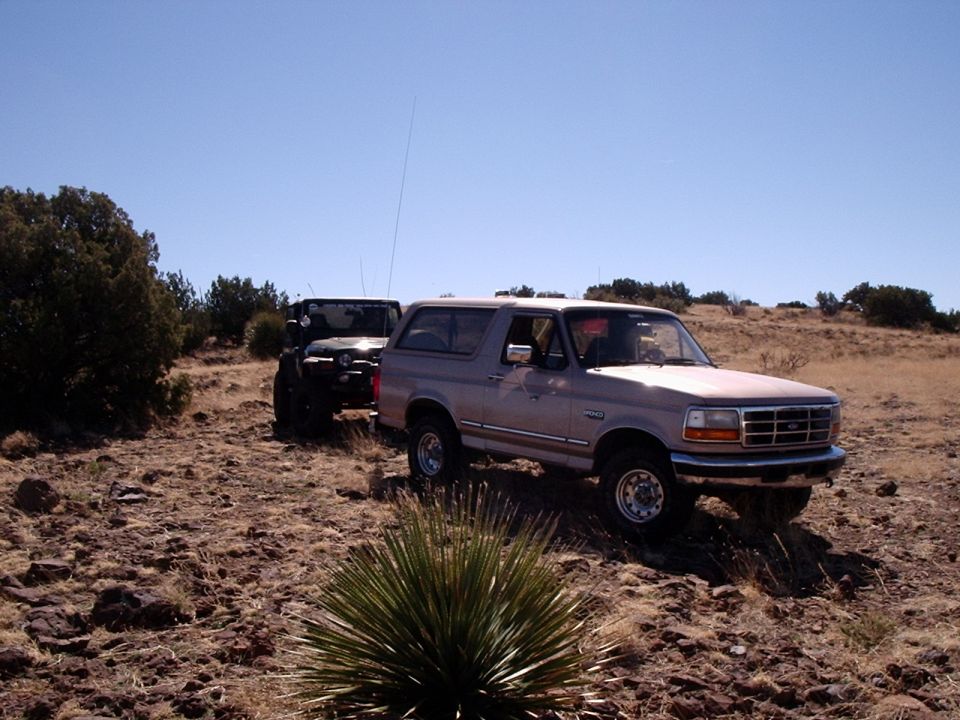 Tan 1992 Ford Bronco parked on a dry, rocky trail next to a black Jeep Wrangler