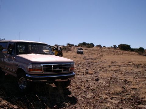 1996 Ford Bronco - Several off-road vehicles navigate a dry, grassy hillside under a clear blue sky.