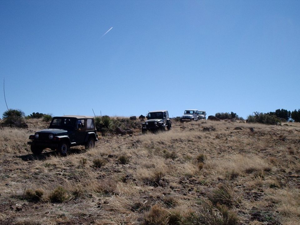 Three Jeeps on a dry, grassy hillside under a clear blue sky